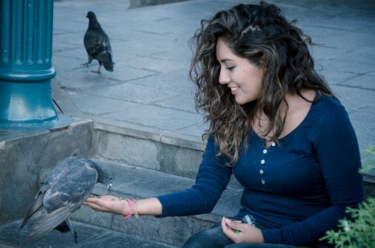 A smiling woman feeding a pigeon from her hand in the park