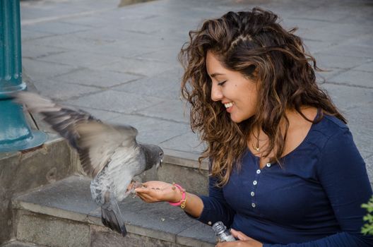 A smiling woman feeding a pigeon from her hand in the park