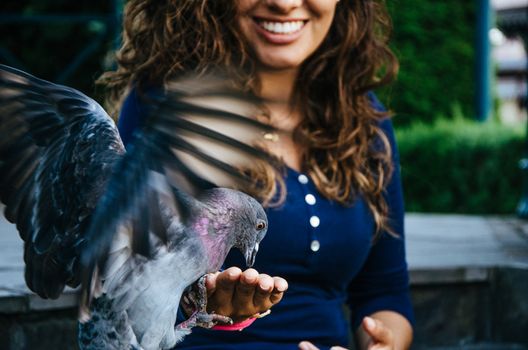 A smiling woman feeding a pigeon from her hand in the park