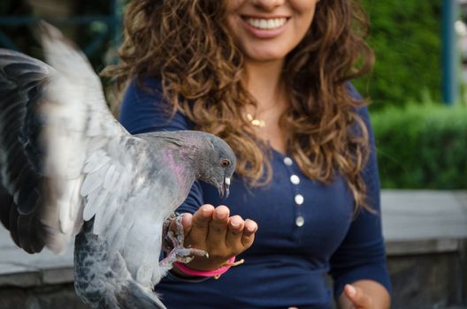 A smiling woman feeding a pigeon from her hand in the park