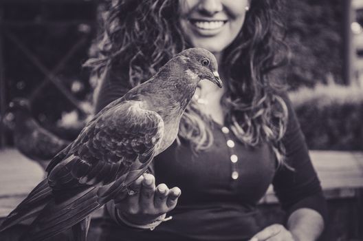 A smiling woman feeding a pigeon from her hand in the park