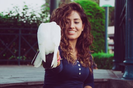 A smiling woman feeding a pigeon from her hand in the park