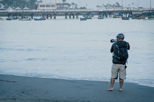 Young photographer with his professional camera taking pictures of boats in the sea, marine background for summer vacations and holiday travel concepts