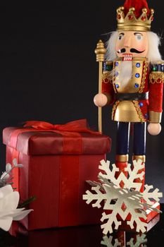A Christmas holiday Nutcracker stands next to a red gift for the season of giving.