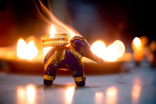 small elephant incense holder with smoke coming out and an out fo focus background with diya oil lamps lit behind it with flickering flames showing the hindu festival of diwali. Shows the beautiful decorations on the hindu festival of diwali where small earthen lamps filled with oil are lit to show the victory of good over evil