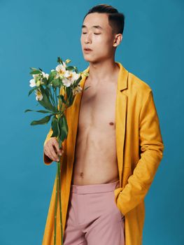A romantic Asian man holds a hand in his pocket and a bouquet of flowers in pink trousers. High quality photo