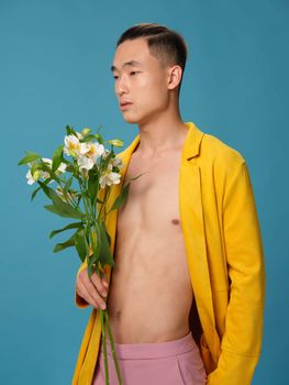 A half-naked guy with a bouquet of white flowers and a yellow coat on a blue background. High quality photo