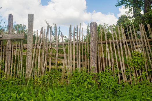 Old rickety wooden fence made of narrow boards in front of village house.