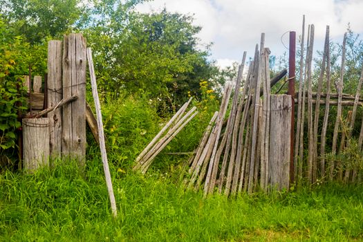 Old rickety wooden fence made of narrow boards in front of village house.