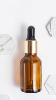 Top view on glass bottles of essential oil or cosmetic serum on white background. Decorative marble and glass hexagons.