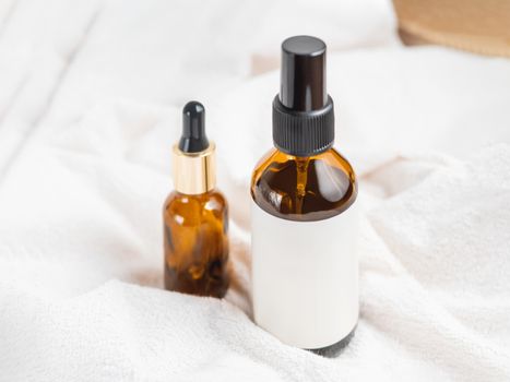 Two glass bottles on white fluffy towel. Essential oil and cosmetic serum with clear labels on crumpled bathrobe. Morning routine.