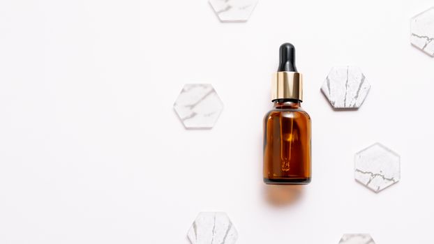 Top view on glass bottles of essential oil or cosmetic serum on white background. White copy space with decorative marble and glass hexagons.