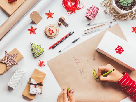 Top view on table with Christmas decorations. Woman draws New Year symbols on craft paper and wraps presents. Flat lay.