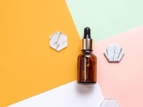 Top view on glass bottles of essential oil or cosmetic serum on colorful geometrical background. Decorative marble and glass hexagons.