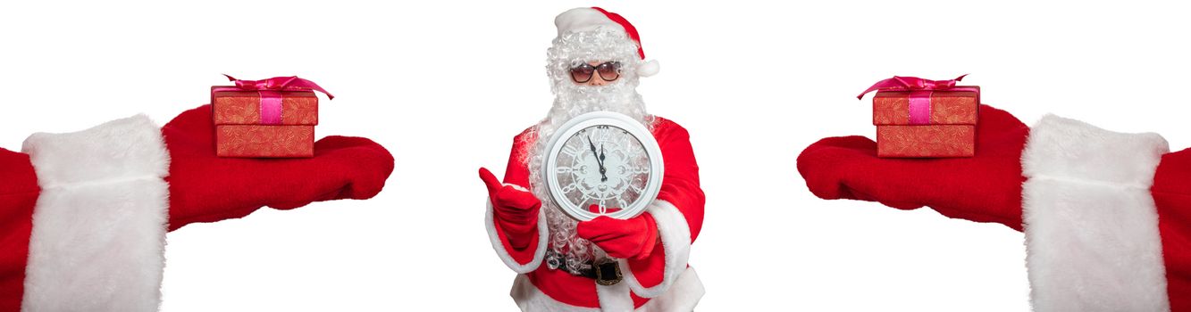 Santa Claus holding a white clock which shows five minutes to midnight. Two hands with gifts on them extended to him. New year's eve concept. Isolated on white background.