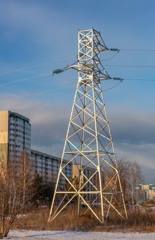 Low angle shot of high voltage electric tower and power lines in the city at sunset. Apartment buildings and blue cloudy sky as a background. Barnaul, Siberia, Russia.