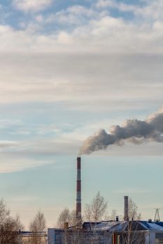 Shot of roof tops and pipes of heating plant that supply central heating system of the city. Smoke coming out of the pipes. Blue cloudy sky as a background. Industrial landscape. Barnaul, Russia.