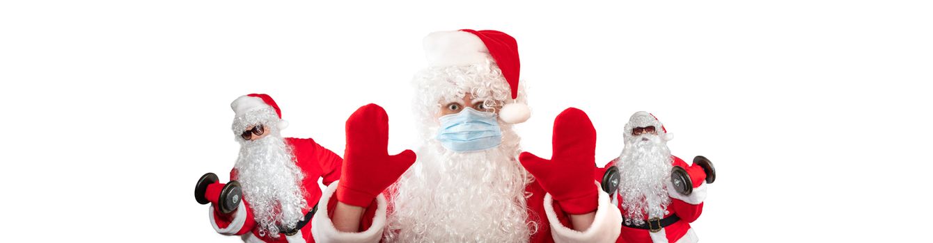 Santa Claus wearing a medical mask, having his both hands up, eyes wide open in warning gesture. Two Santa Clauses working out in the background behind him. Isolated on white background. Banner size, copy space.