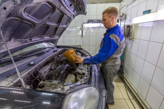 Car mechanic replacing and pouring oil into engine at car service station during regular check-up routine.