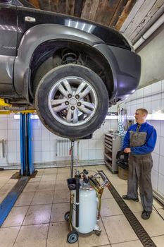 Car mechanic changes oil in a workshop. Mechanic standing next to the car and draining oil into a special cannister. Car is on the hydraulic lift.