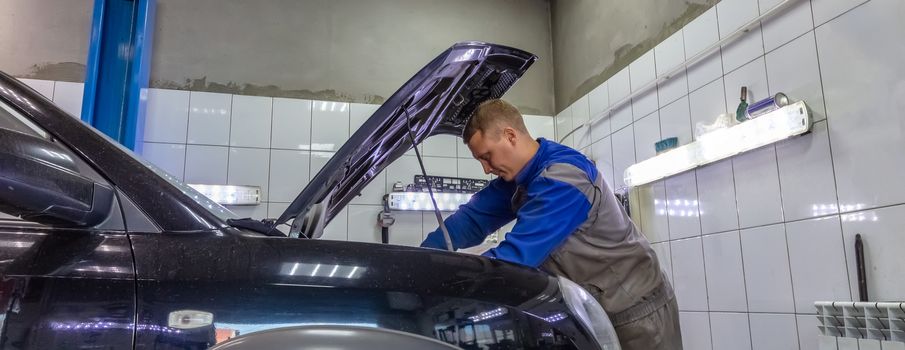 An auto mechanic under the hood, working on a car engine. Mechanic looks very serious and concentrated.