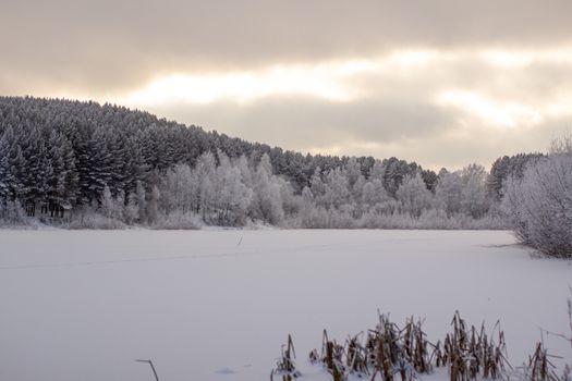 Dramatic sky with clouds over the winter forest and lake. Winter and frosty nature. Frozen lake near the forest, all covered in snow.