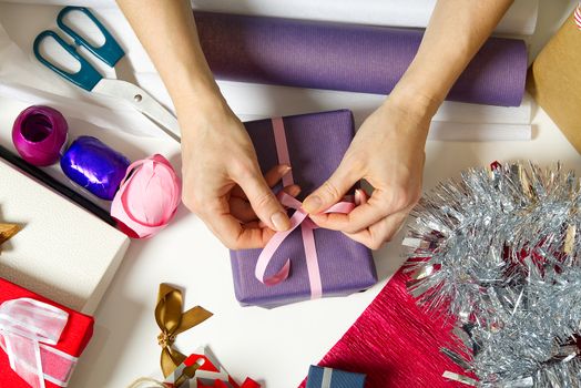 Woman wrapping christmas presents to violet packing paper. woman hands packing a christmas gift, diy gift packing and wrapping concept.