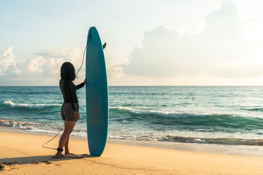 Surfer woman carrying their surfboards on sunset beach with sun light  background