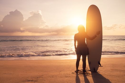 Silhouette of surfer woman carrying their surfboards on sunset beach with sun light  background