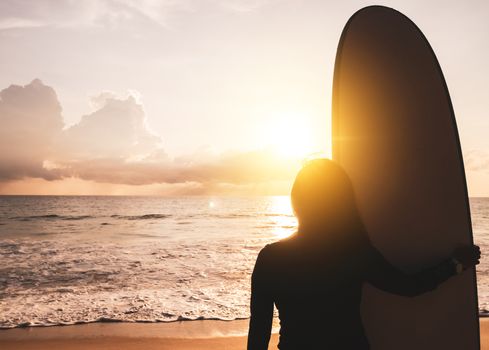 Silhouette of surfer woman carrying their surfboards on sunset beach with sun light  background