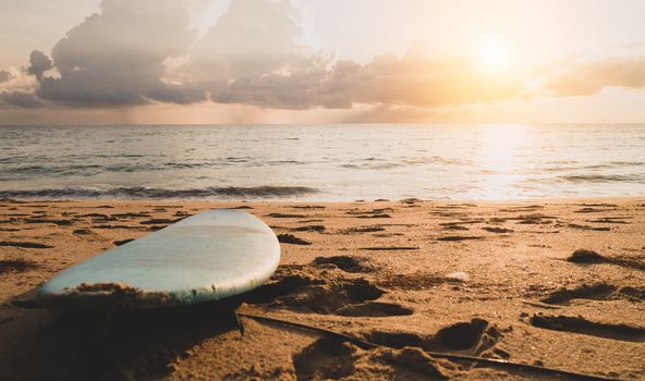 Surfboard on sand at summer beach with sunset light background.