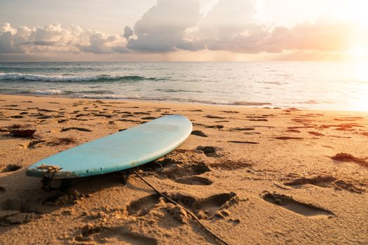 Surfboard on sand at summer beach with sunset light background.