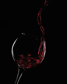 Splash of red wine in a glass on a black background close-up