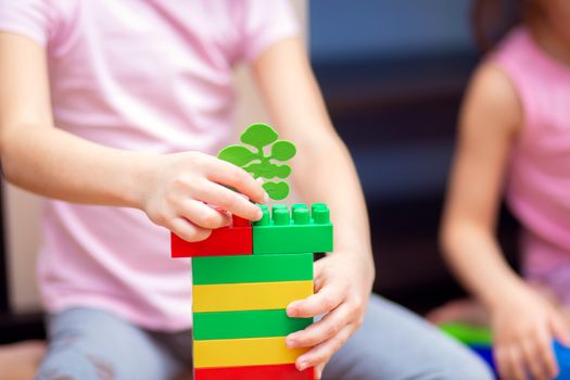 A little girl at home plays with a plastic colored constructor. A child built a tower from parts of a children's designer