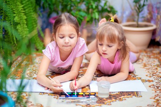 Two girls paint with paints lying on the floor at home or in kindergarten. Home leisure