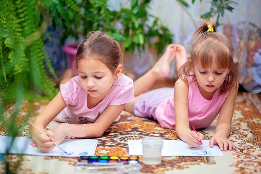 Two girls paint with paints lying on the floor at home or in kindergarten. Home leisure