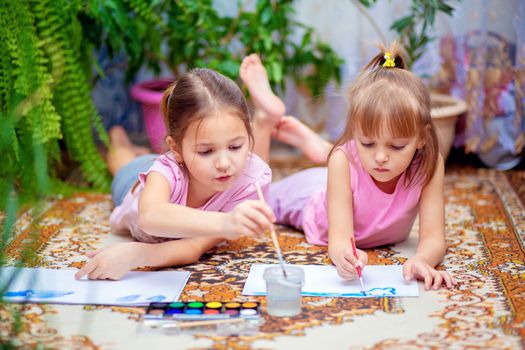 Two girls paint with paints lying on the floor at home or in kindergarten. Home leisure