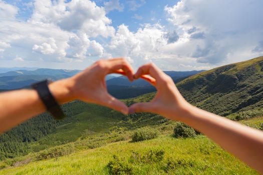 Male and female hand folded heart against the sky. Traveling in the Carpathians.