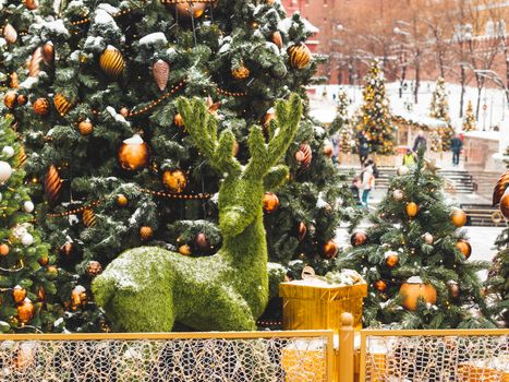Christmas tree with golden and bronze balls and reindeer made of artificial grass. Outdoor decorations for New Year celebration. Moscow, Russia.