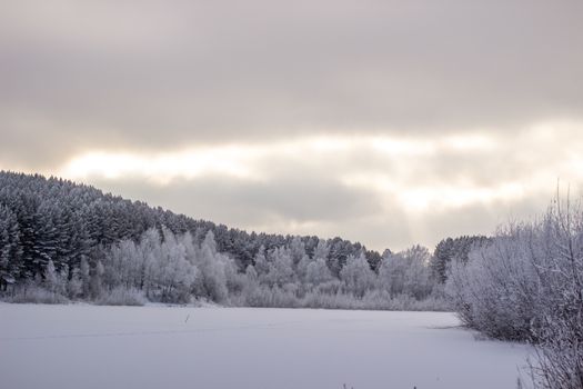 Dramatic sky with clouds over the winter forest and lake. Winter and frosty nature. Frozen lake near the forest, all covered in snow.