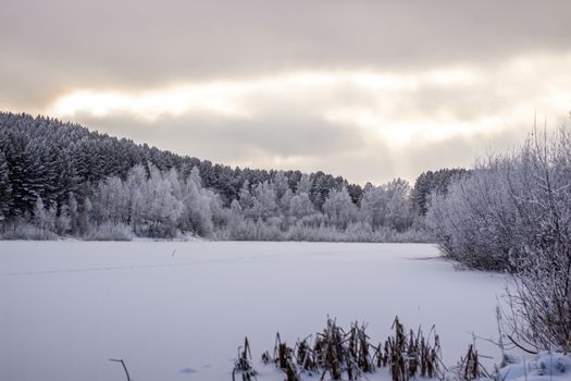 Dramatic sky with clouds over the winter forest and lake. Winter and frosty nature. Frozen lake near the forest, all covered in snow.