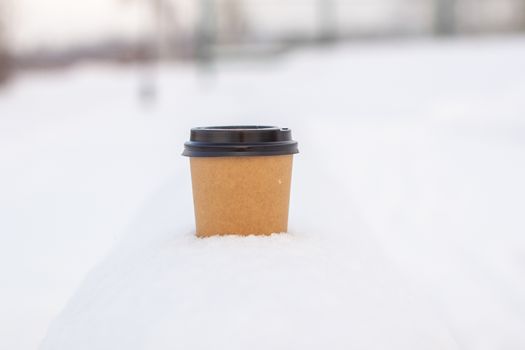 Cardboard coffee Cup in the snow in winter. Hot drink tea or coffee in a glass in winter outside.