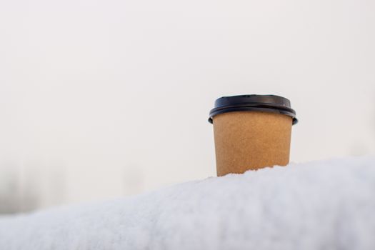 Cardboard coffee Cup in the snow in winter. Hot drink tea or coffee in a glass in winter outside.