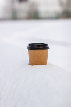 Cardboard coffee Cup in the snow in winter. Hot drink tea or coffee in a glass in winter outside.