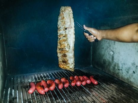 Hand grabbing a piece of meat cooking on a grill.
