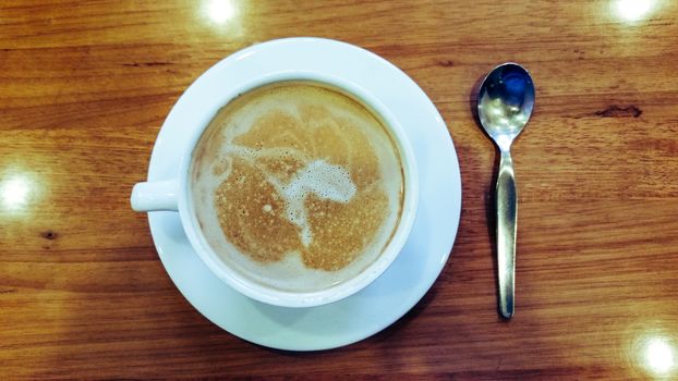 Top view of espresso cup, spoon and an illuminated wooden background