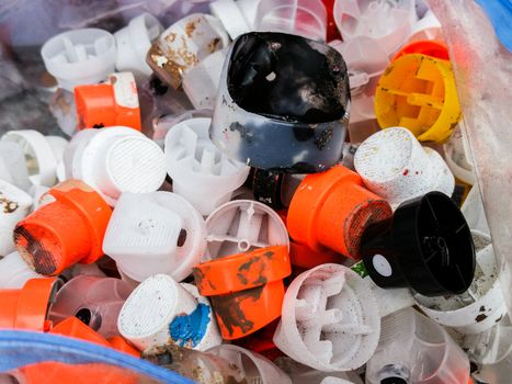 Many plastic caps of sprays to make urban art in front of a painted wall in colored graffiti drawings.
