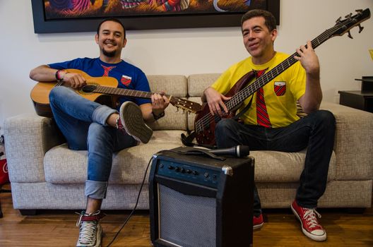 Young smiling people playing guitars sitting on a sofa at home with an amplifier