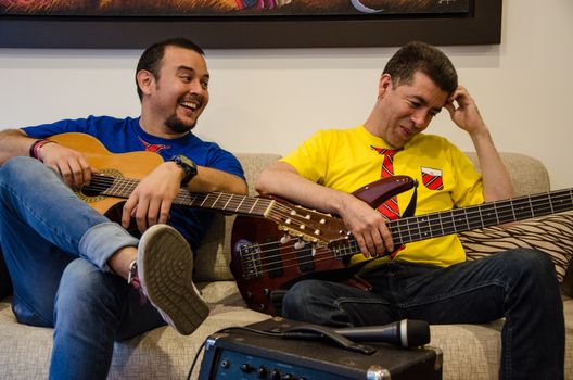 Young smiling people playing guitars sitting on a sofa at home