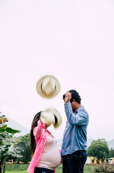 Future mom and couple with plaid shirt outdoors throwing hats